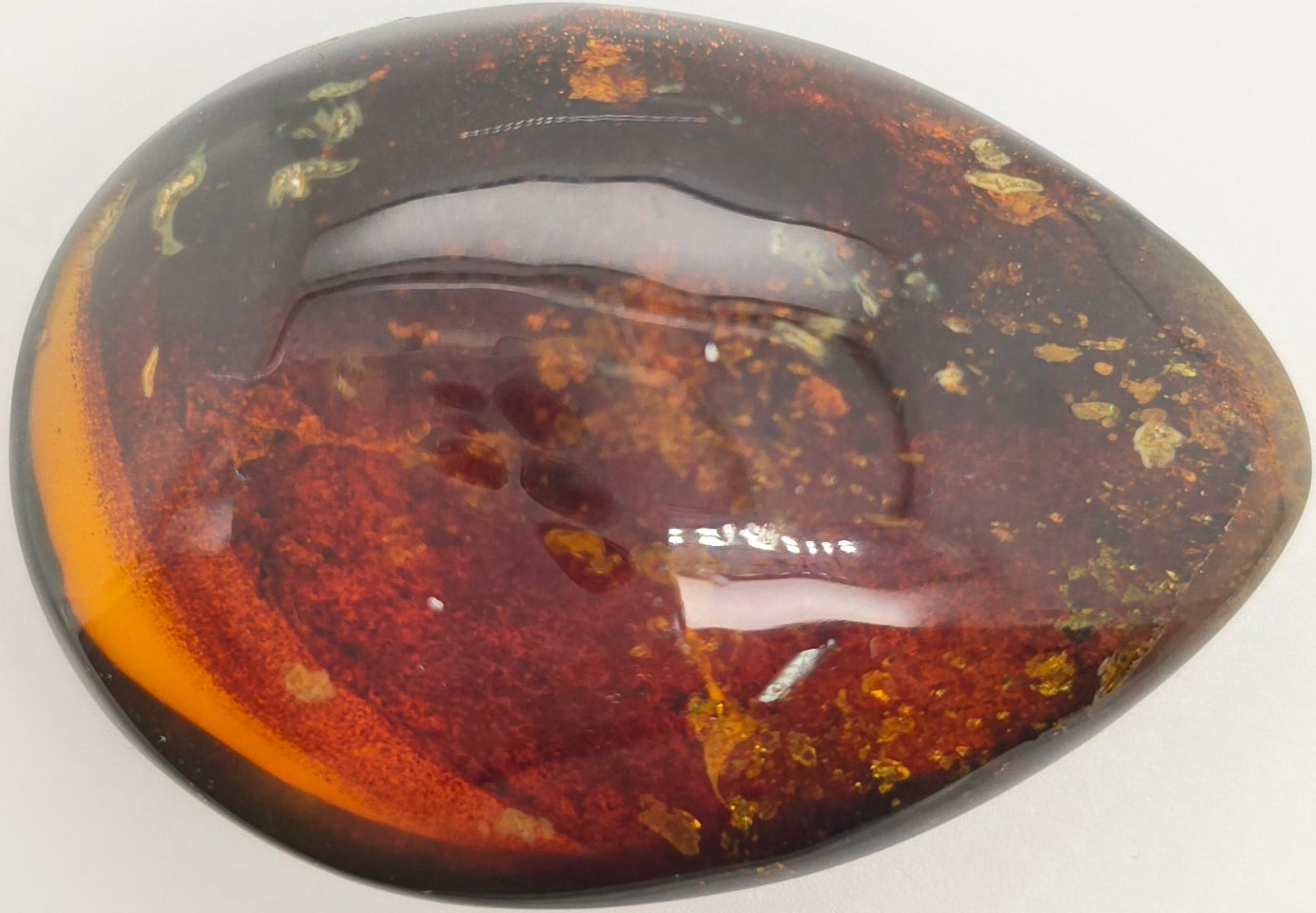 A polished teardrop-shaped gemstone with a smooth, glossy surface, featuring a marbled pattern of deep reddish-brown, amber orange with inclusions on a plain white background.