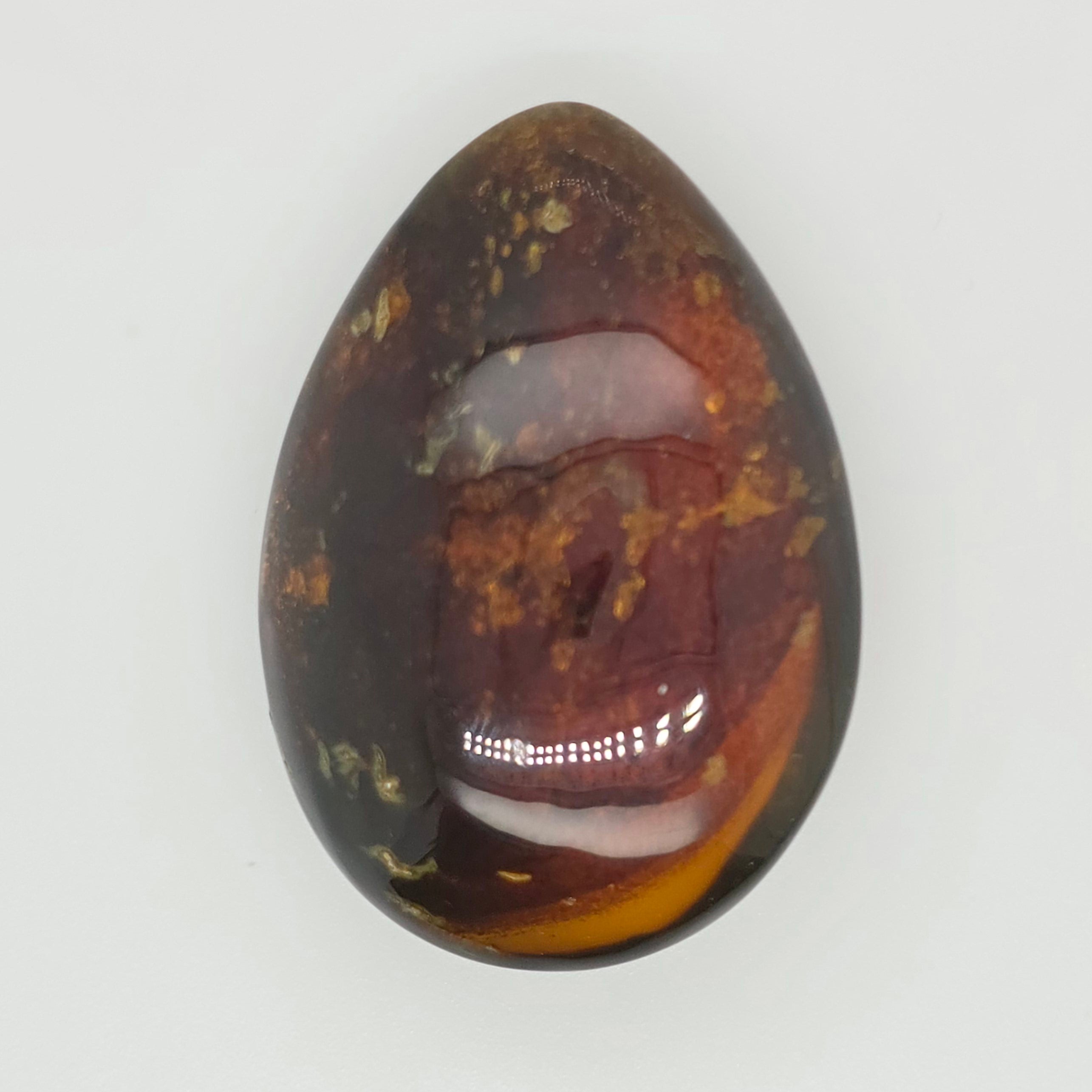 A polished teardrop-shaped cabochon gemstone with a marbled pattern of dark brown, reddish-brown, amber, and black, set against a plain light gray background.