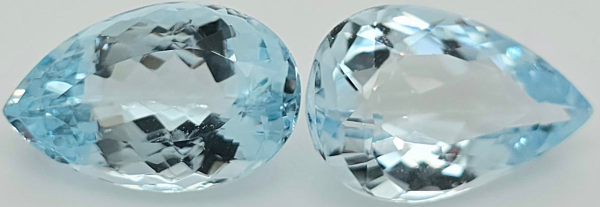 Two pear shaped faceted light blue gemstones side by side on a plain white background