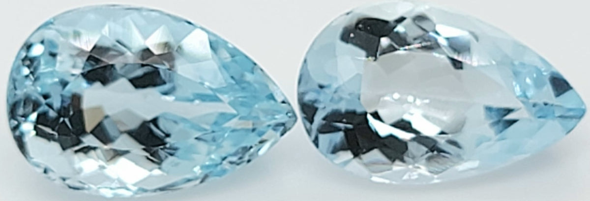 Two light blue pear shaped faceted gemstones side by side on a plain white background