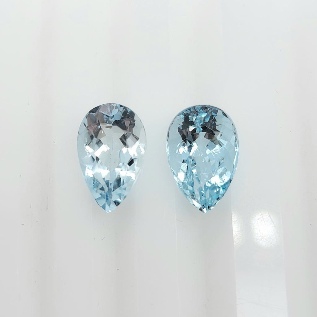 Two pear shaped faceted light blue gemstones side by side on a plain white background