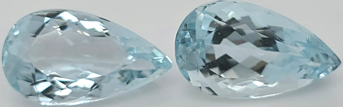 Two light blue pear shaped faceted gemstones side by side on a plain white background