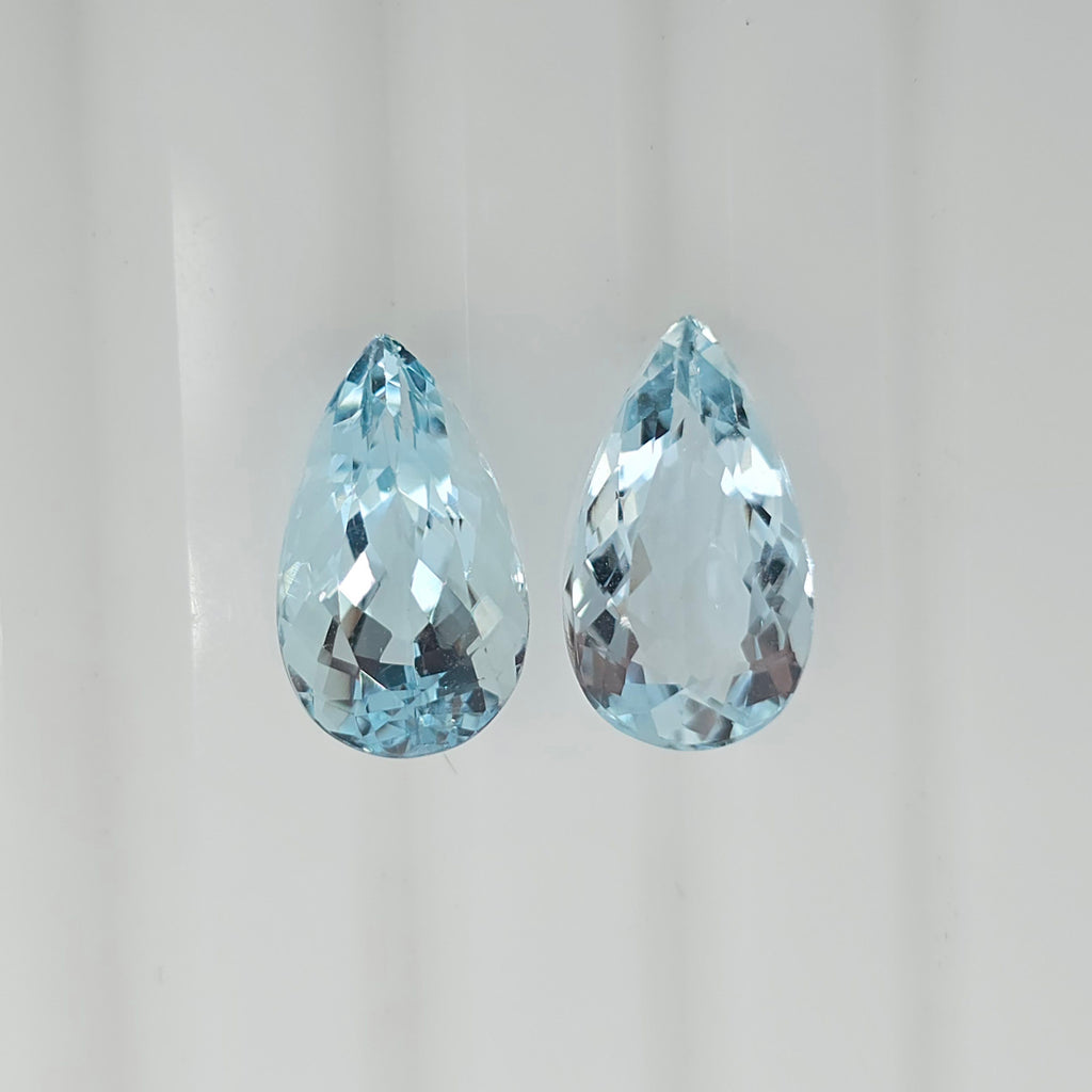 Two pear shaped light blue faceted gemstones side by side on a plain white background