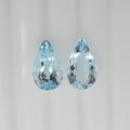 Two pear shaped light blue faceted gemstones side by side on a plain white background