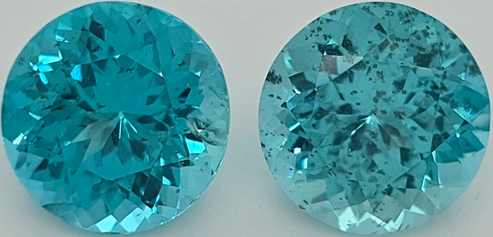 Two round brilliant-cut turquoise-blue gemstones shown side by side on a plain light background.