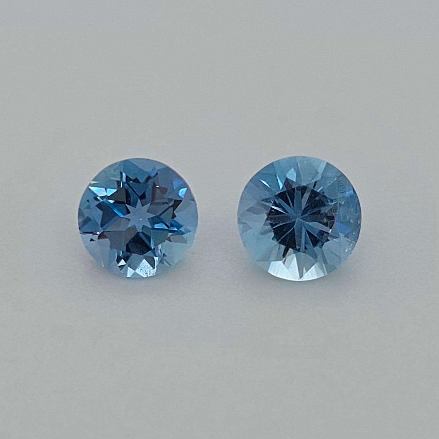 Two round-cut blue gemstones displayed side-by-side on a neutral light gray background