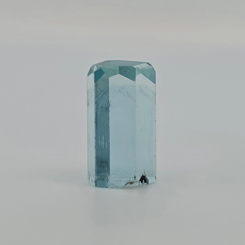 A light blue aquamarine crystal, standing upright on a neutral light gray surface.