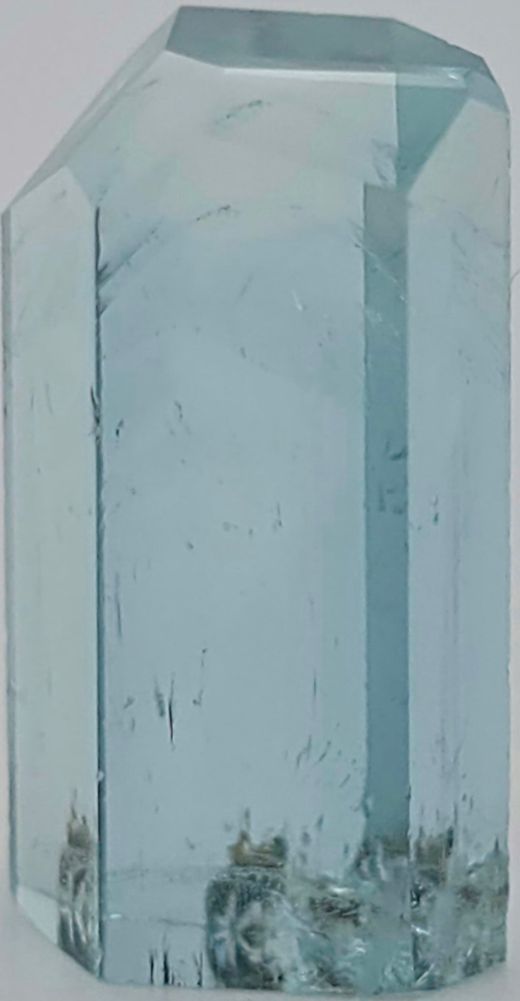 A transparent light blue crystal with internal inclusions photographed against a plain light background.