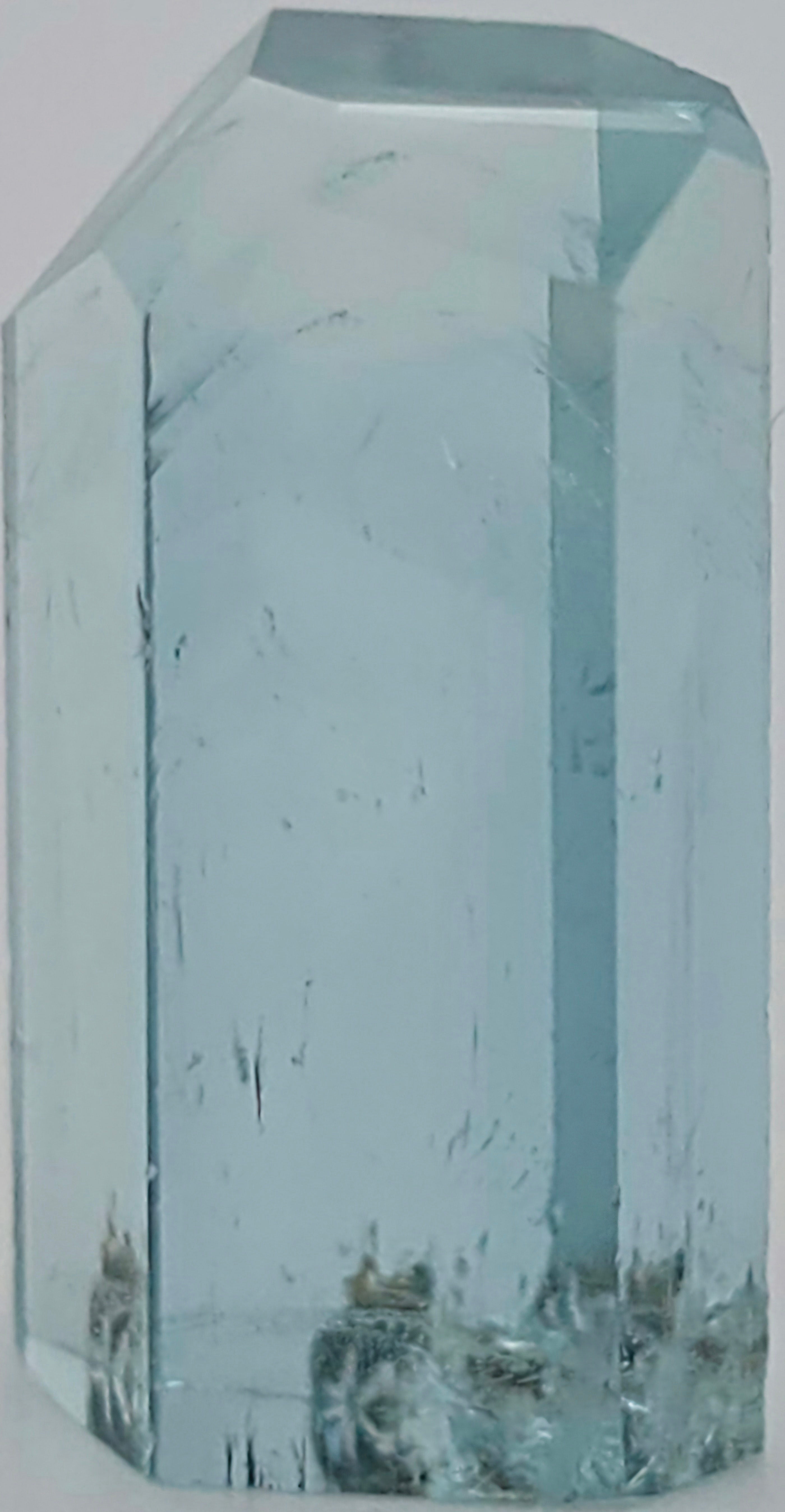 A transparent light blue crystal with internal inclusions photographed against a plain light background.