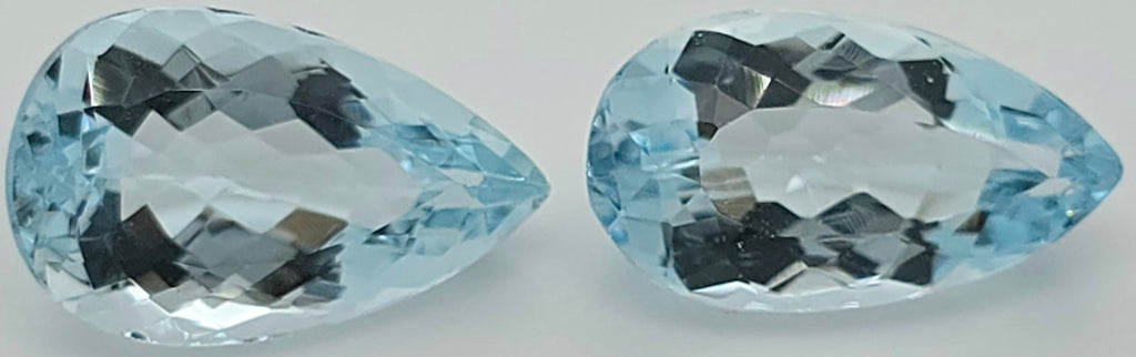 Two pear shaped faceted light blue gemstones side by side on a plain white background