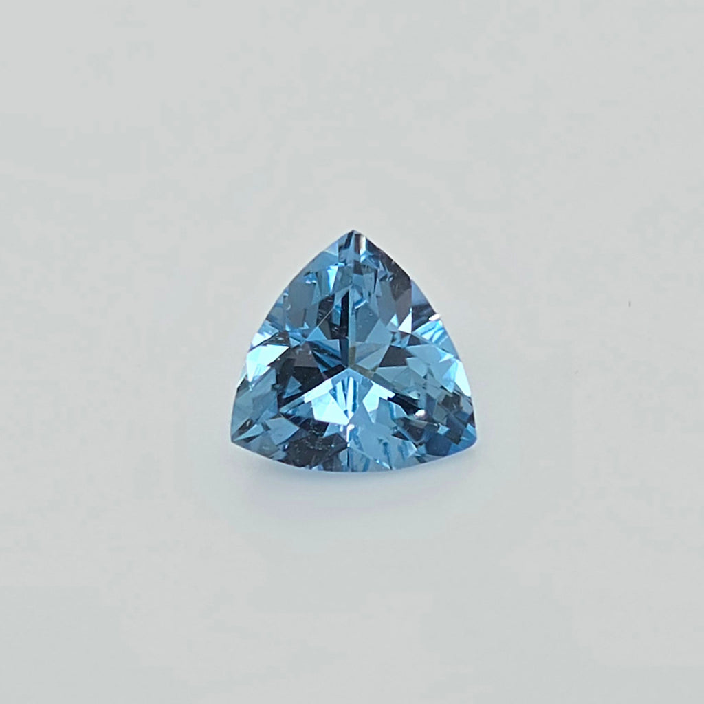 A single faceted triangular blue gemstone, centered on a plain light gray background.