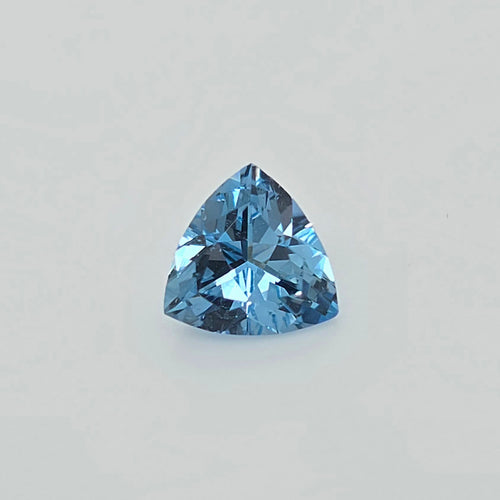 A single faceted triangular blue gemstone, centered on a plain light gray background.