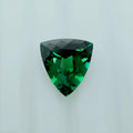 A faceted triangular green gemstone shown on a plain light gray background.
