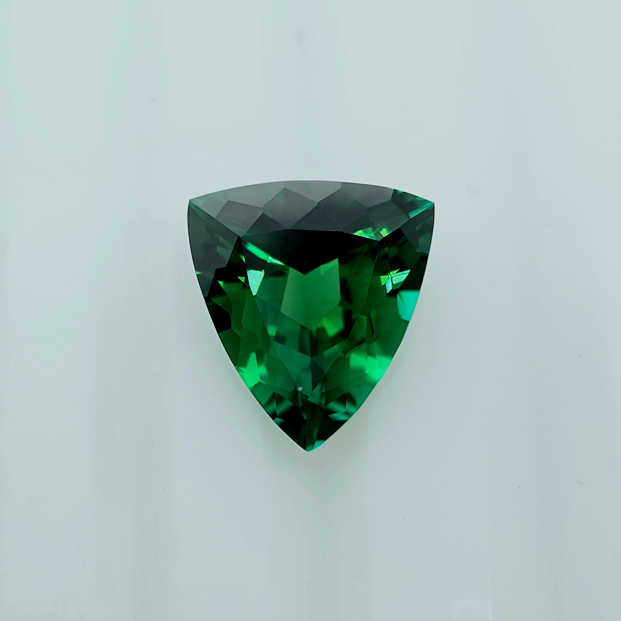 A faceted triangular green gemstone shown on a plain light gray background.