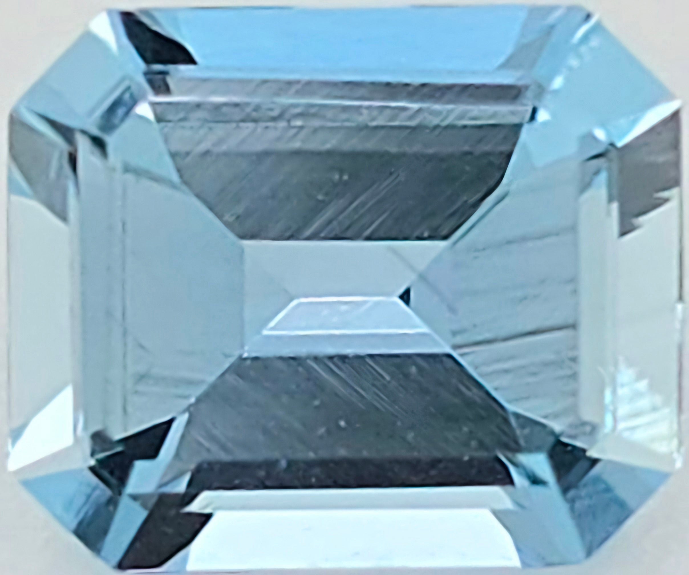 A close up of a light blue emerald cut gemstone against a white background