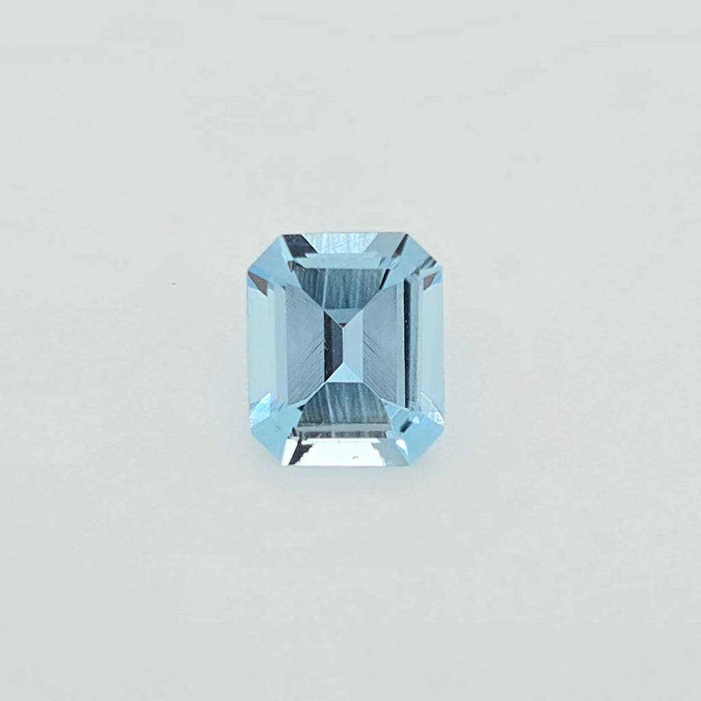 A single light blue emerald-cut faceted gemstone centered on a plain light gray background.
