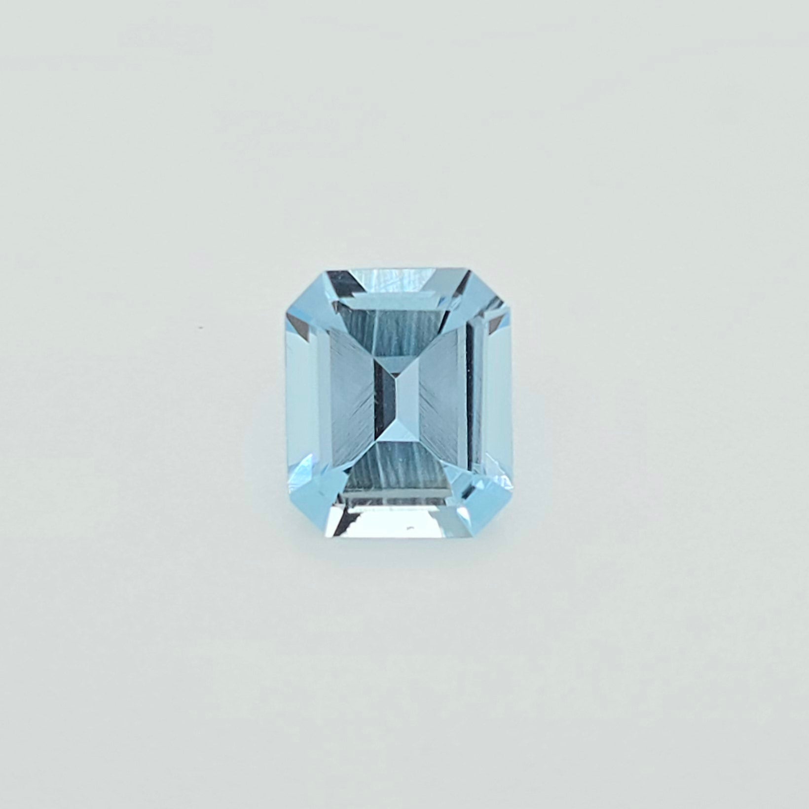 A single light blue emerald-cut faceted gemstone centered on a plain light gray background.