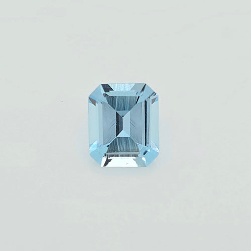 A single light blue emerald-cut faceted gemstone centered on a plain light gray background.