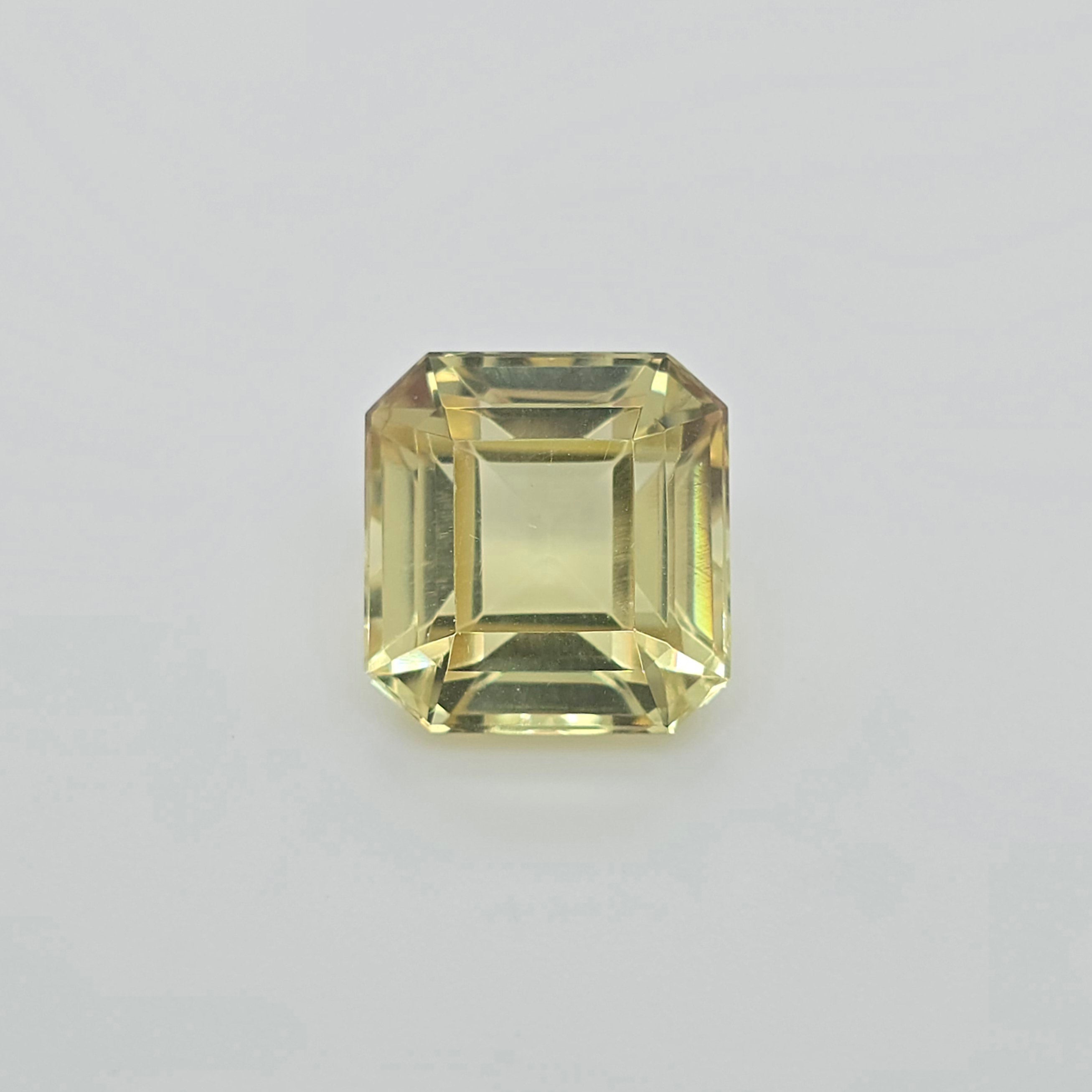 A single square emerald-cut yellow gemstone with faceted edges, centered on a light gray background.