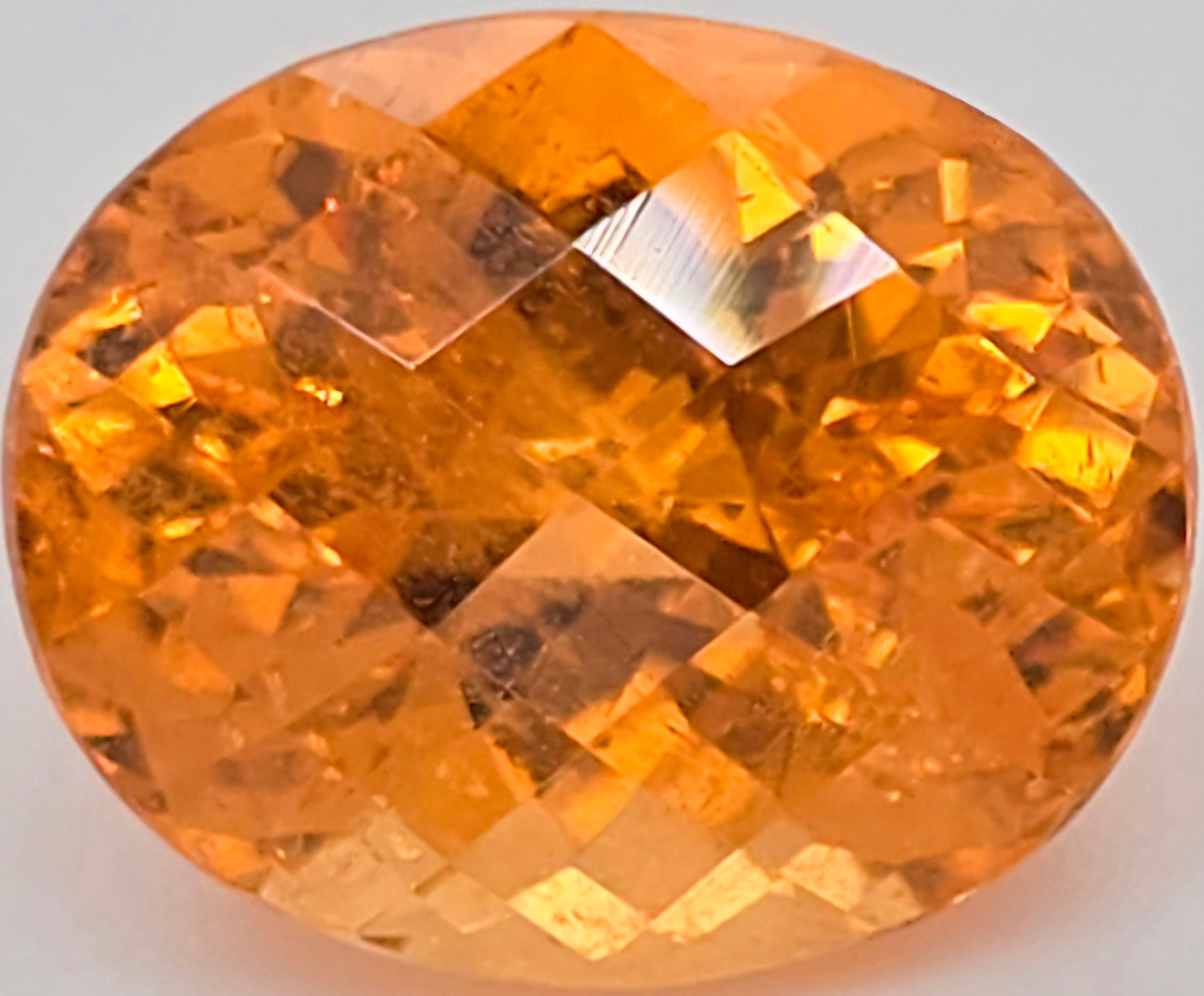 An oval-cut faceted orange gemstone, showing vibrant yellow-orange and amber tones with reflective highlights, set against a plain light background.