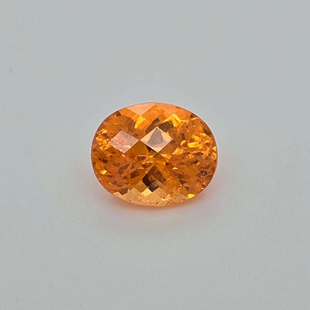 An oval-cut orange gemstone with a faceted, diamond-cut pattern, centered on a light gray background.