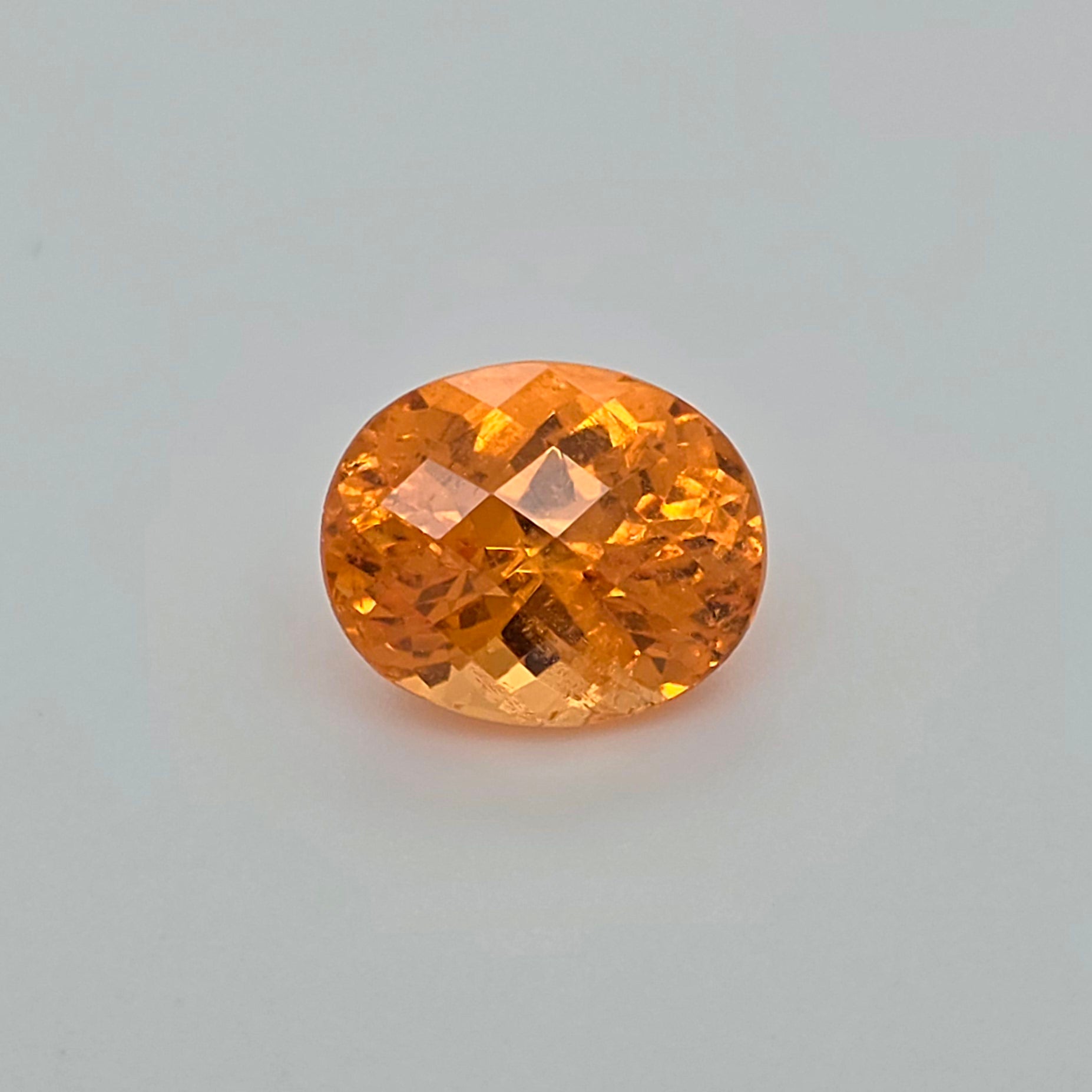 An oval-cut orange gemstone with a faceted, diamond-cut pattern, centered on a light gray background.