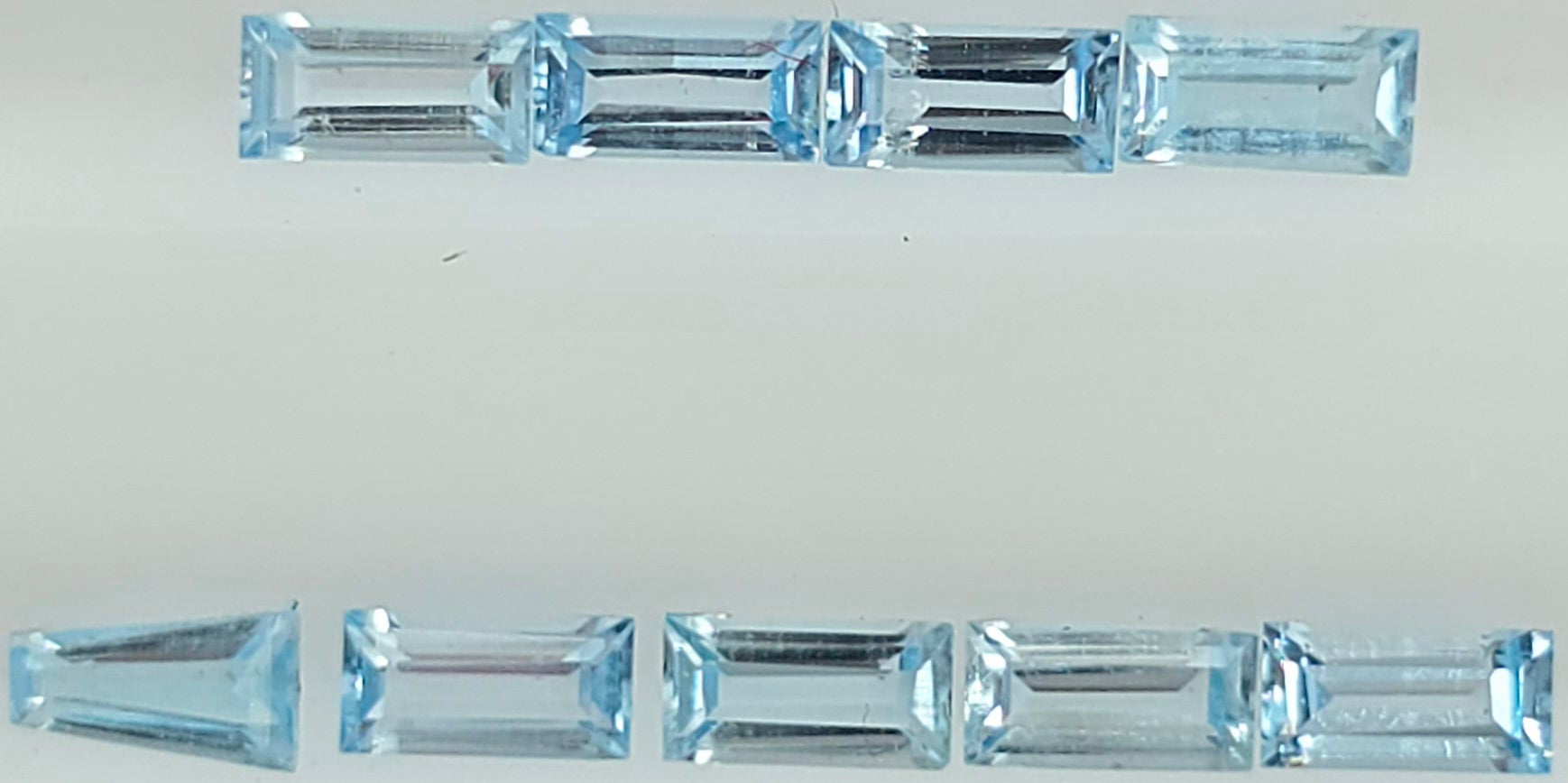 Nine light blue rectangular baguette-cut gemstones arranged in two rows on a plain white background.