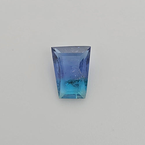 A trapezoid shaped gemstone with a blue to turquoise gradient, displayed on a neutral light gray background.