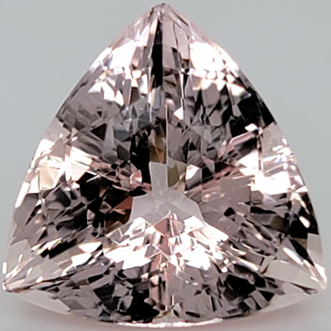 A triangular brilliant-cut diamond with a pink hue, showing intricate facets and reflections against a neutral light gray background.