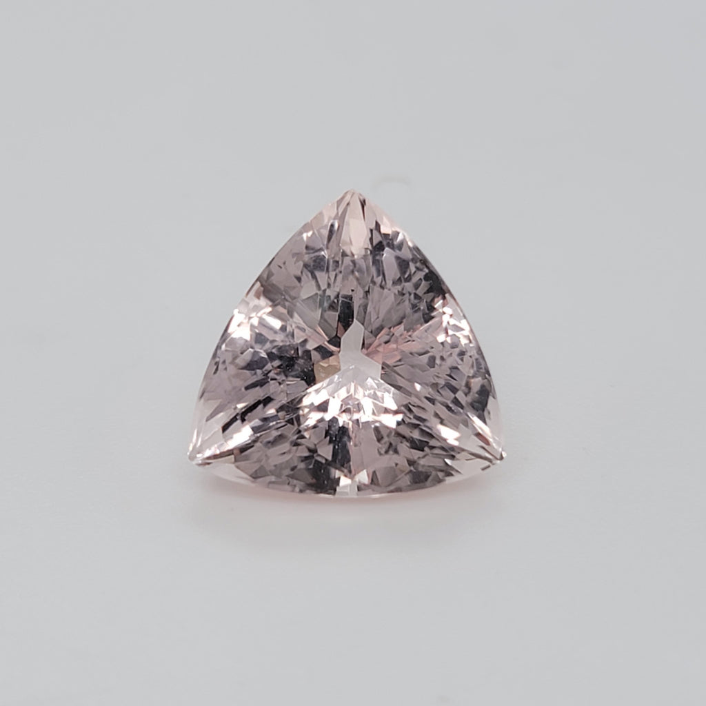 A triangular cut pink gemstone with brilliant faceting, centered on a light gray background.
