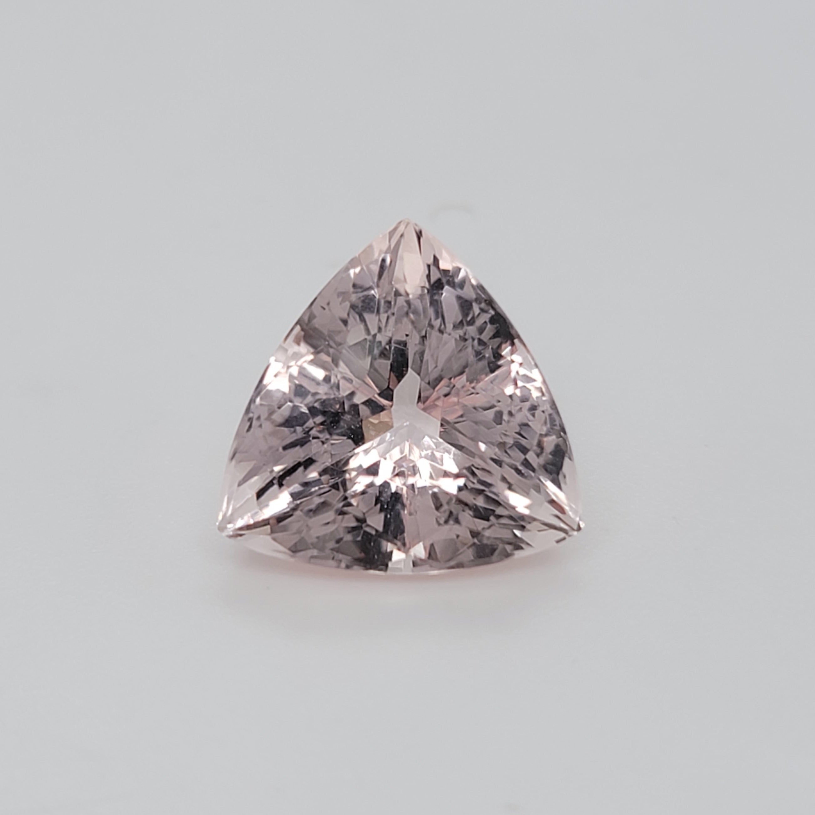 A triangular cut pink gemstone with brilliant faceting, centered on a light gray background.