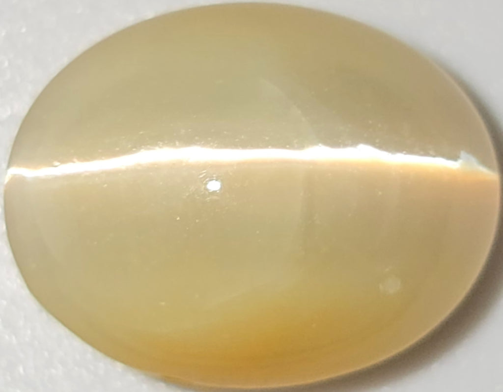 A smooth, oval-shaped cabochon gemstone with a creamy, translucent pale yellow color and a horizontal band of bright white reflection.