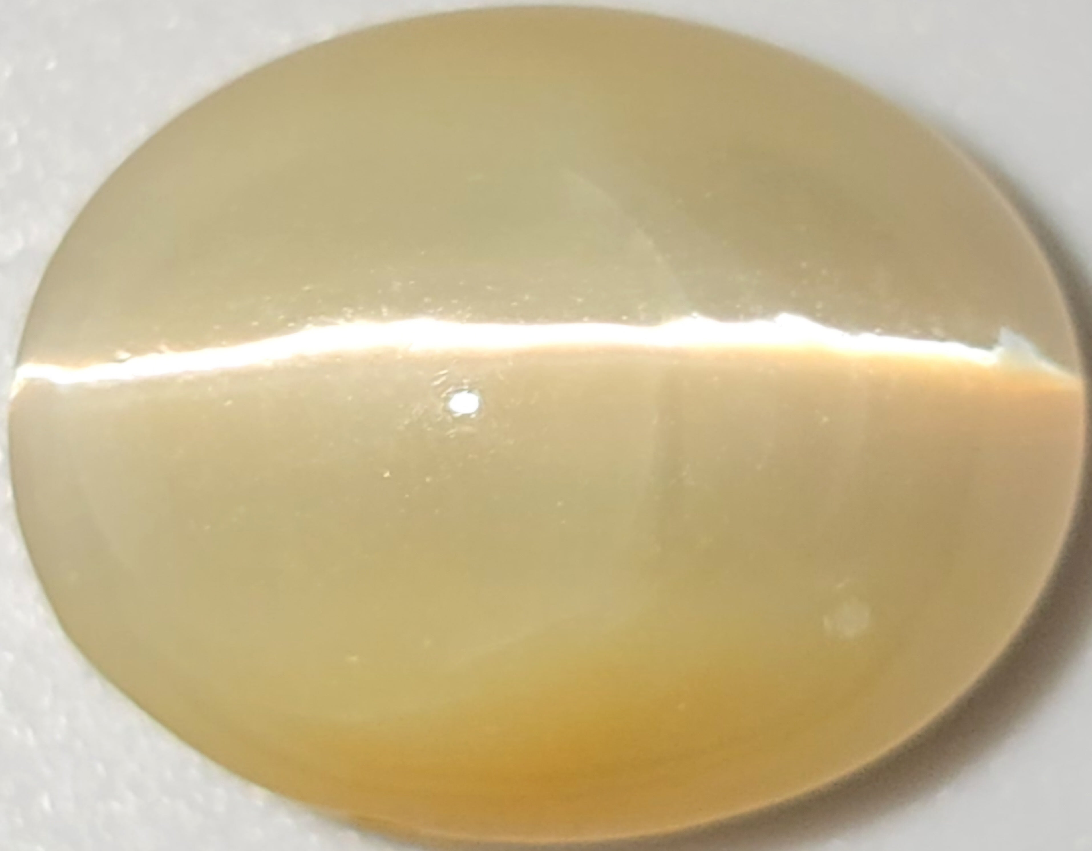 A smooth, oval-shaped cabochon gemstone with a creamy, translucent pale yellow color and a horizontal band of bright white reflection.