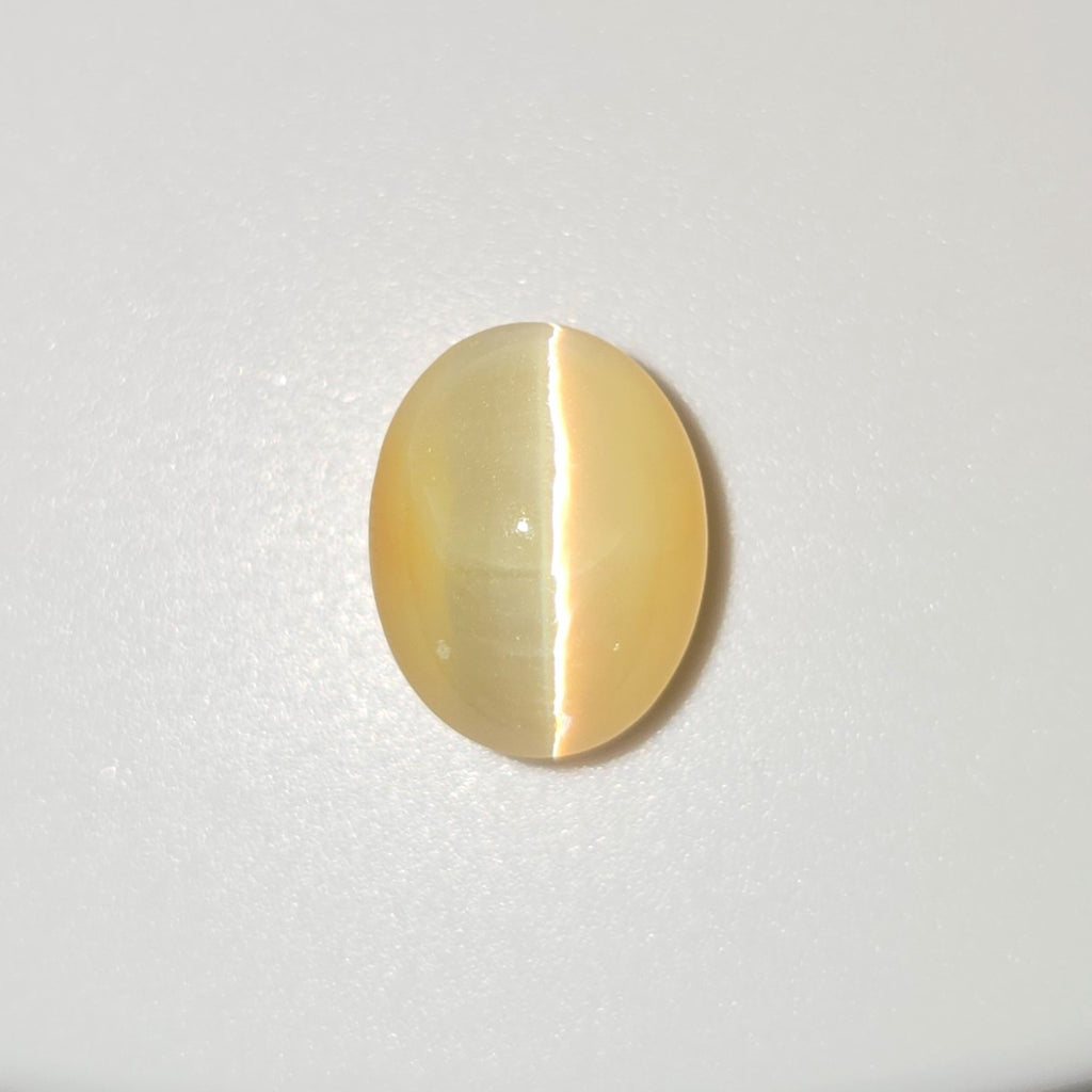 An oval cat's eye gemstone with a pale yellow body and a distinct white split reflection, displayed on a clean white background.