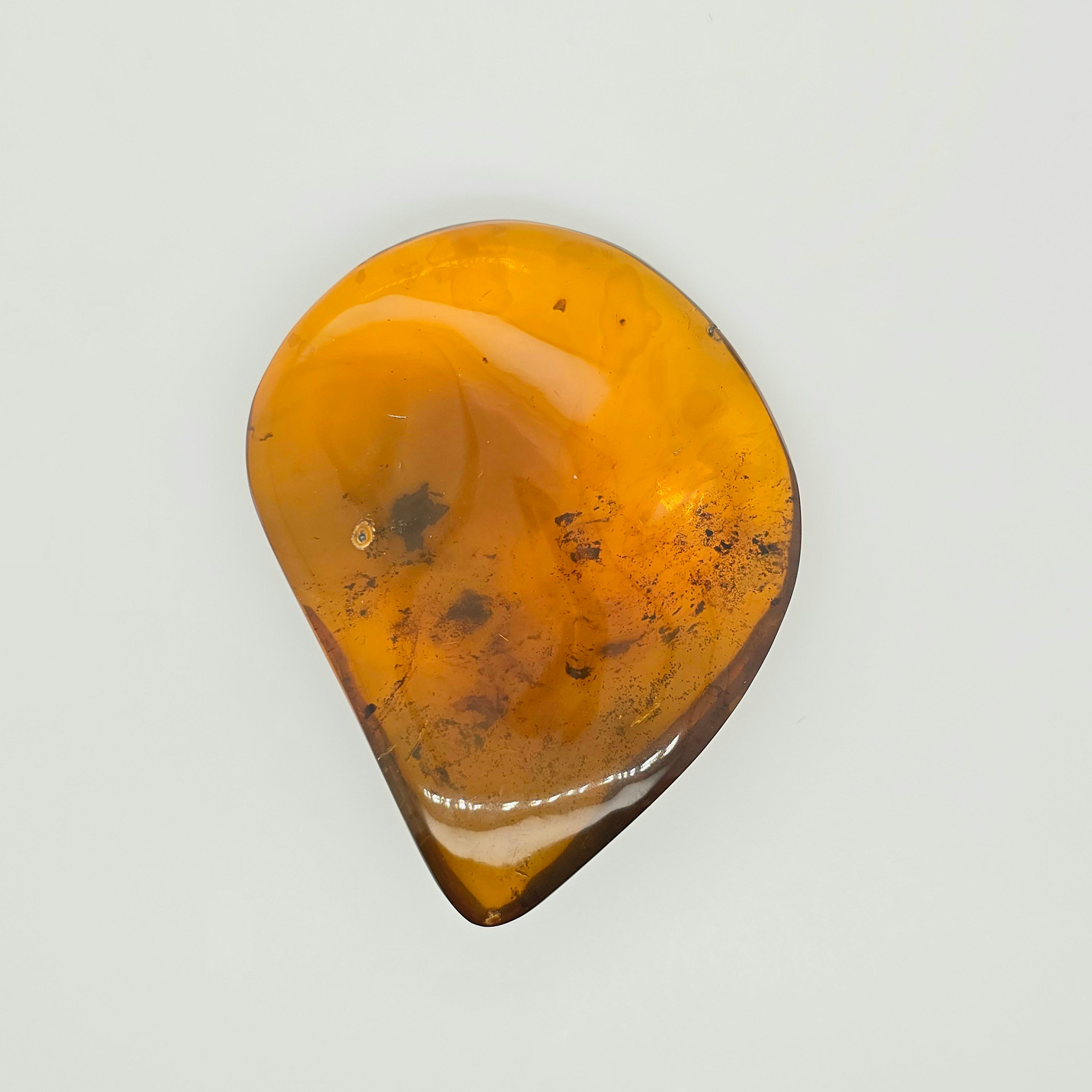 A polished teardrop-shaped amber stone with natural inclusions, displayed on a clean, light off-white background.