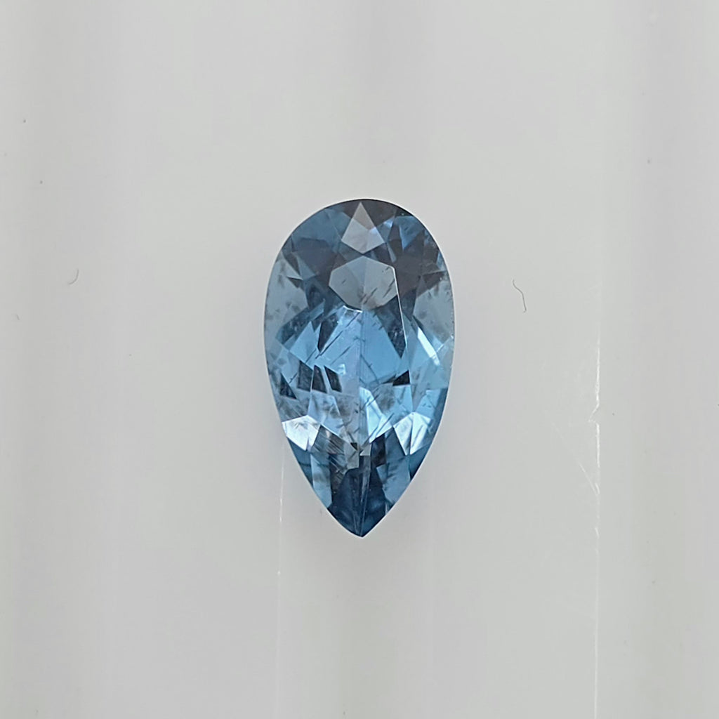 A single pear-shaped blue gemstone with a faceted cut, centered on a plain light gray background.
