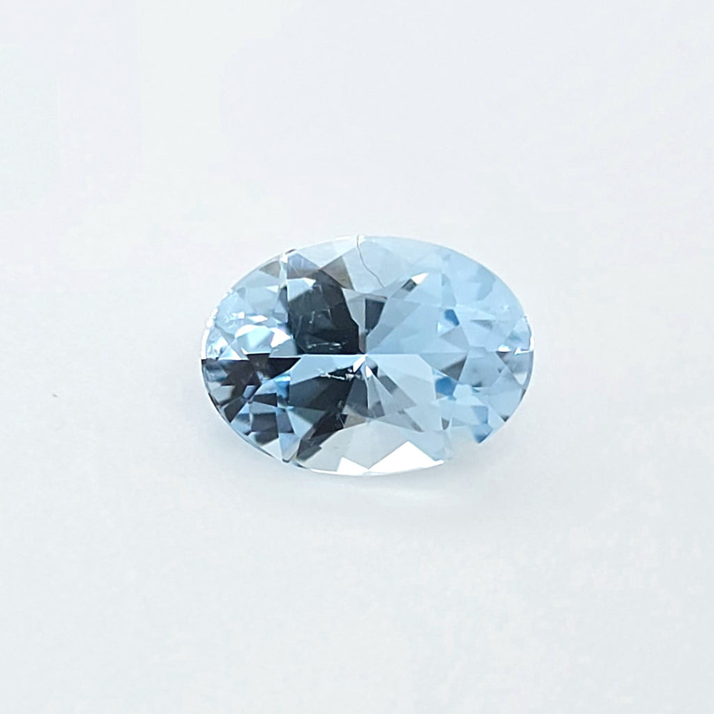 An oval-cut light blue gemstone with a faceted, brilliant cut, displayed on a clean white background.