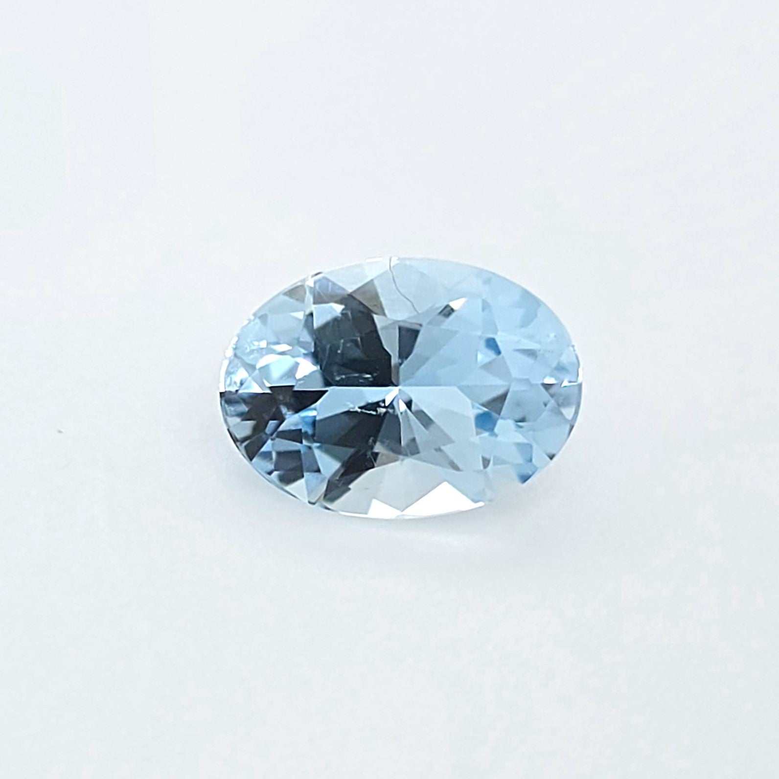 An oval-cut light blue gemstone with a faceted, brilliant cut, displayed on a clean white background.