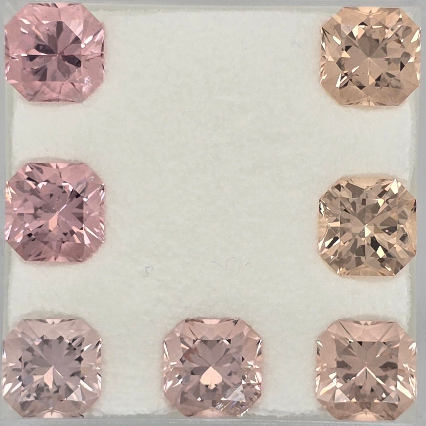 Seven faceted square-cut gemstones arranged in a U-shape on a white textured background. Four stones are light pink, and three are peachy pink with warm golden-brown undertones.