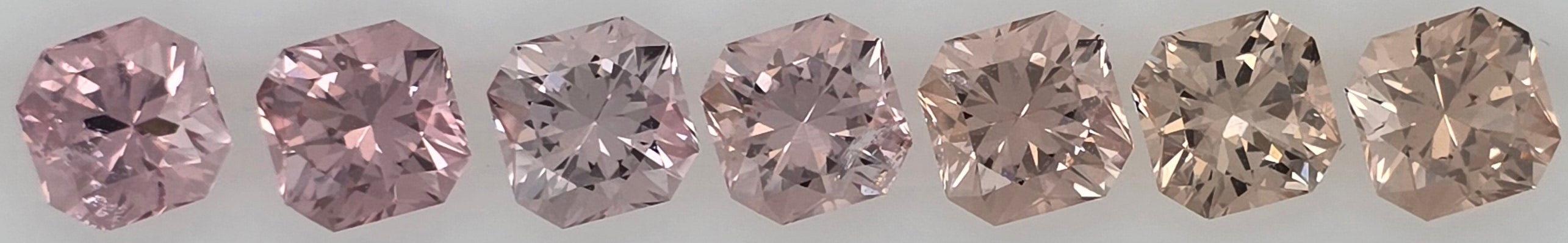 Seven loose square-cut pink to pinkish orange gemstones displayed side-by-side on a plain white background.