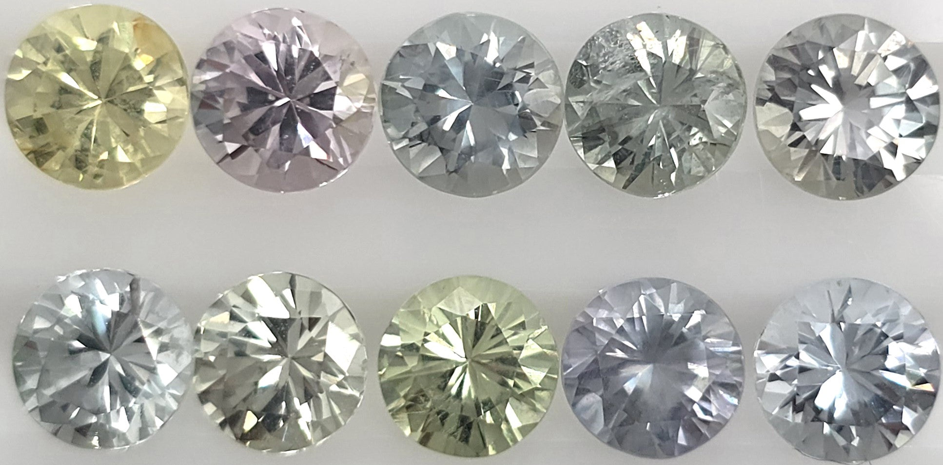 Ten faceted round gemstones arranged in two rows on a white background, showing a mix of silver, green, pink, and yellow tones.