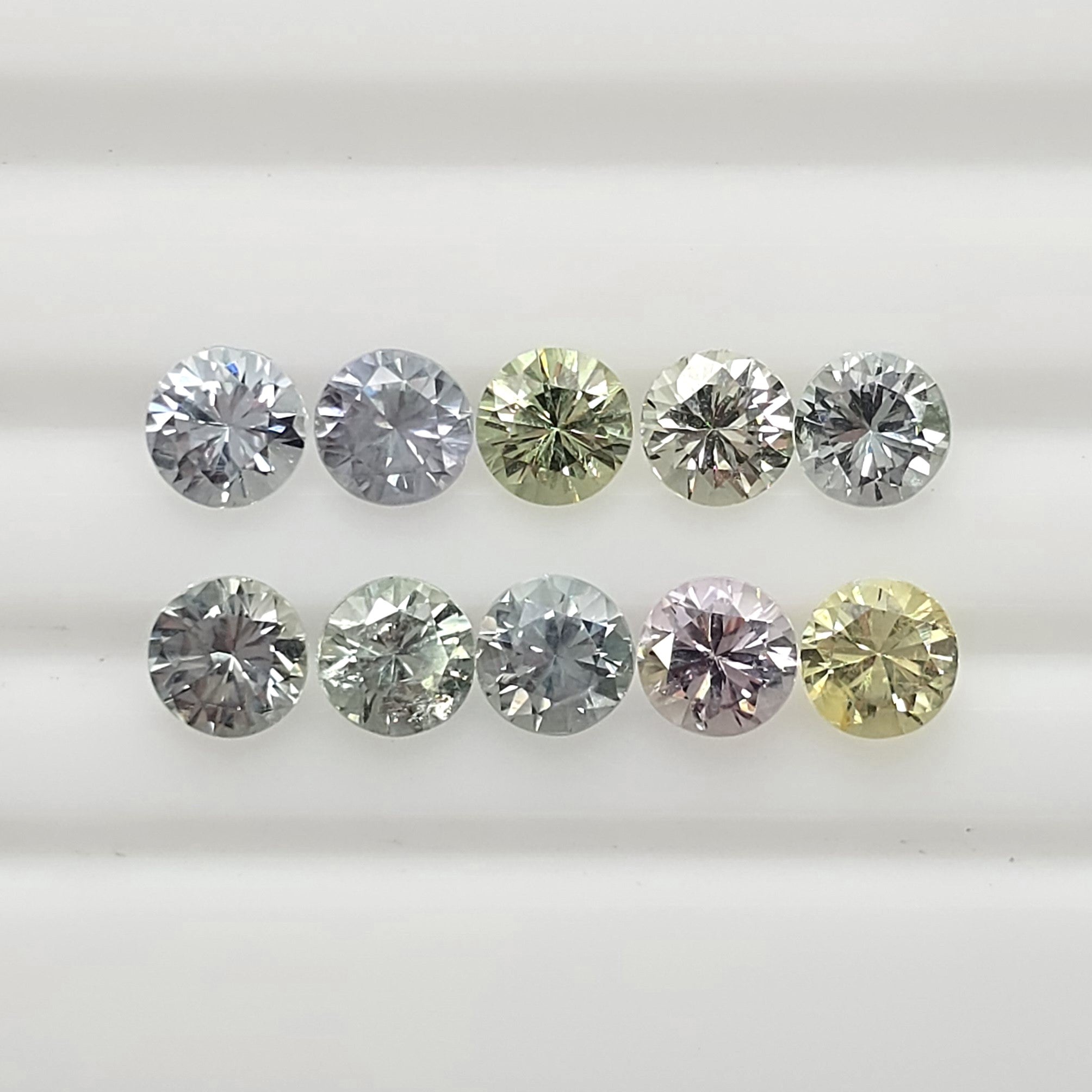 Ten faceted round gemstones arranged in two rows on a white background, showing a mix of silver, green, pink, and yellow tones.