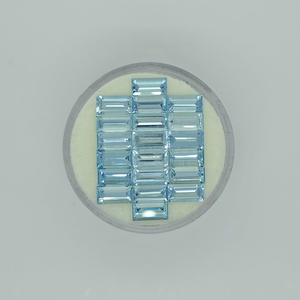 Twenty rectangle cut light blue faceted stones arranged in three columns on a circular off-white pad on a white background