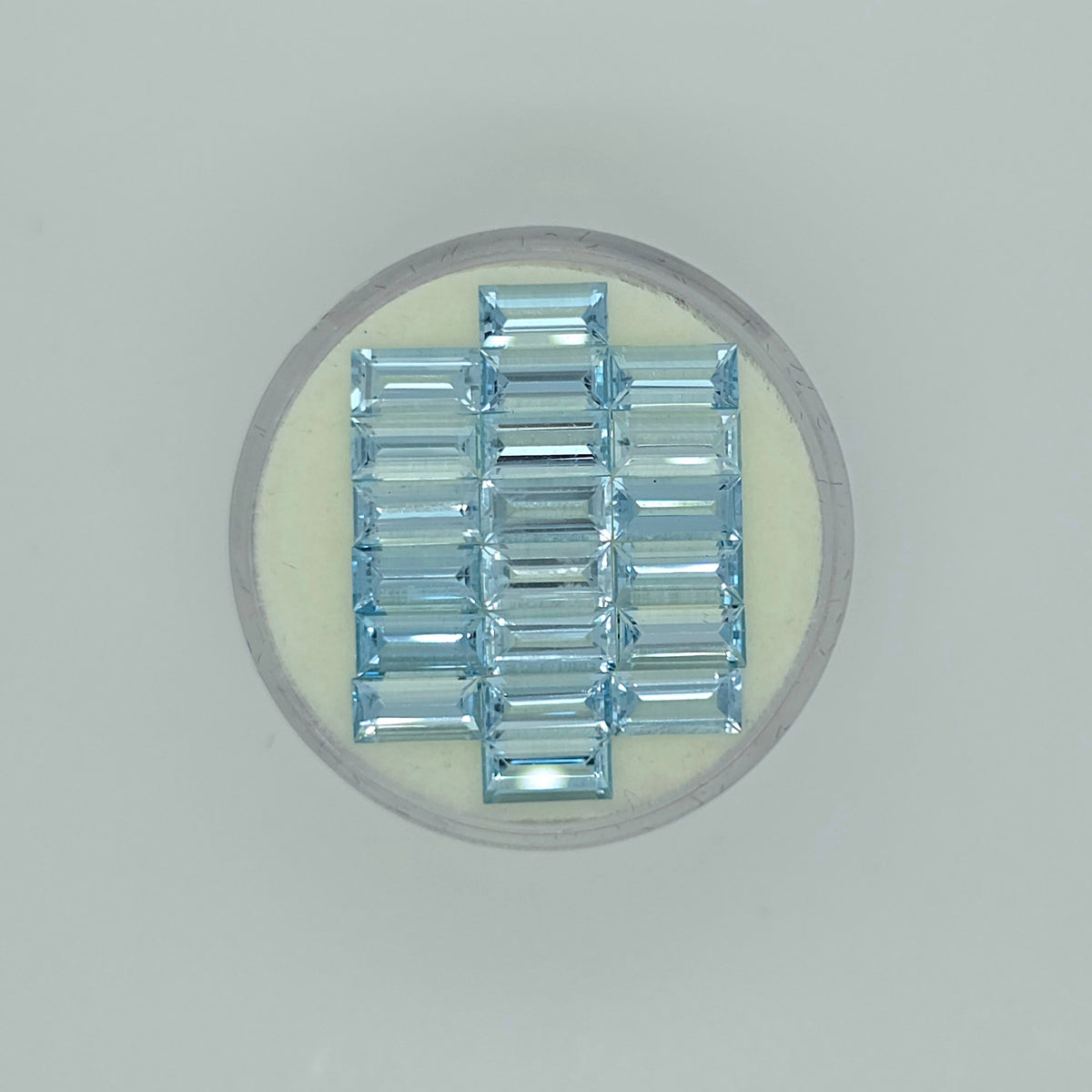 Twenty rectangle cut light blue faceted stones arranged in three columns on a circular off-white pad on a white background