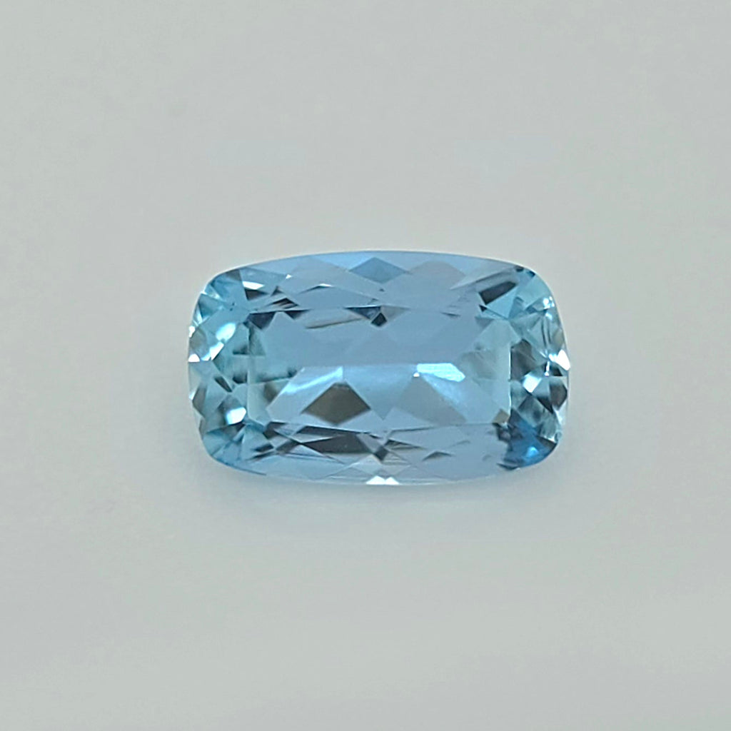 A light blue cushion-cut faceted gemstone centered on a plain light gray background.