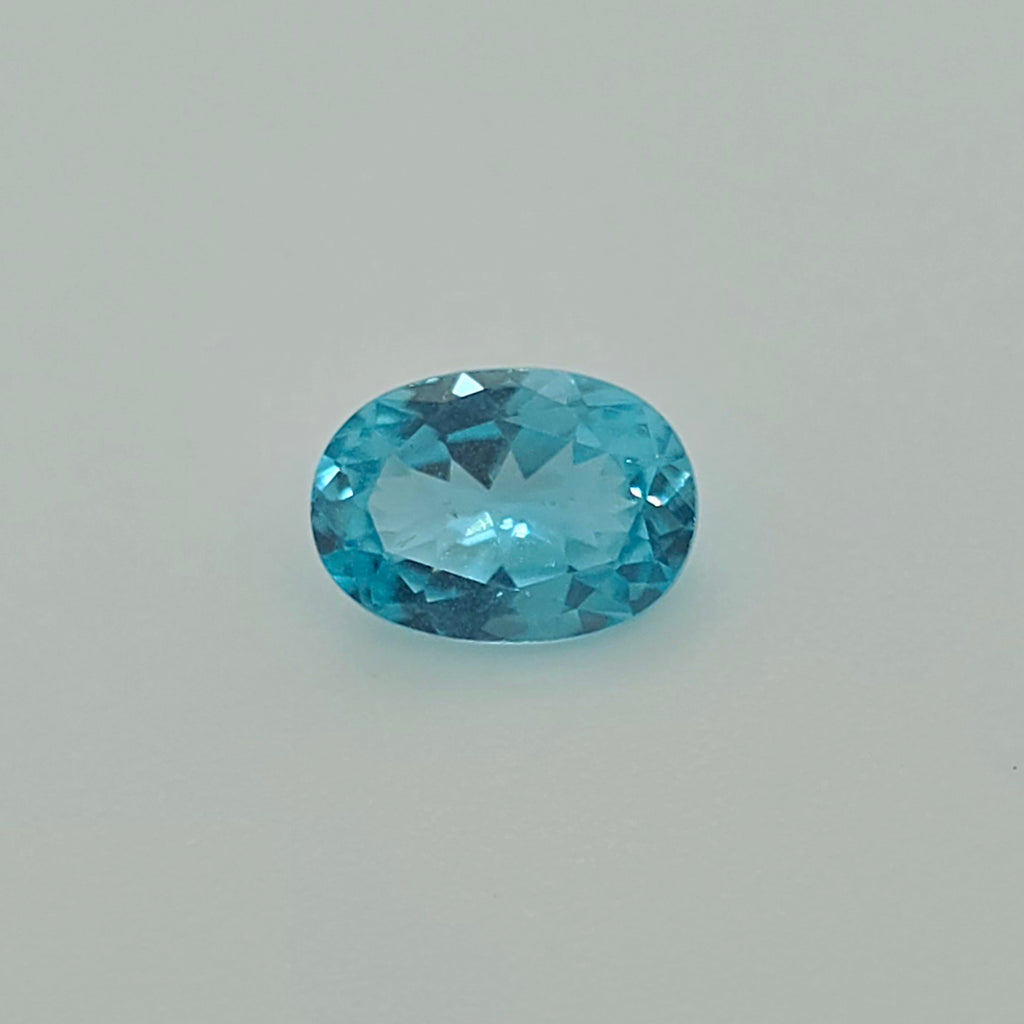 A faceted oval-cut greenish blue gemstone centered on a plain light gray background.