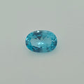 A faceted oval-cut greenish blue gemstone centered on a plain light gray background.