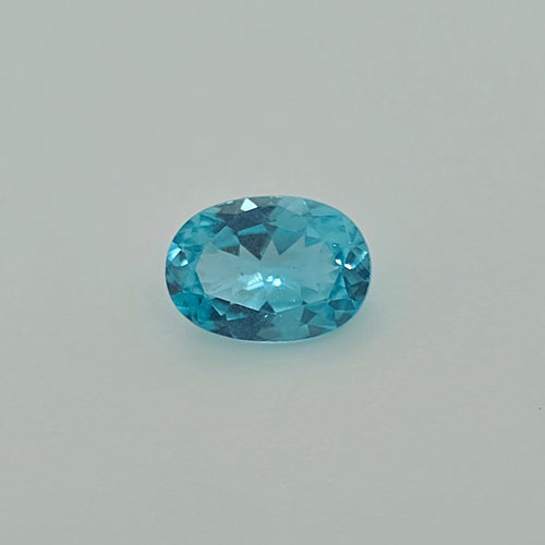 A faceted oval-cut greenish blue gemstone centered on a plain light gray background.