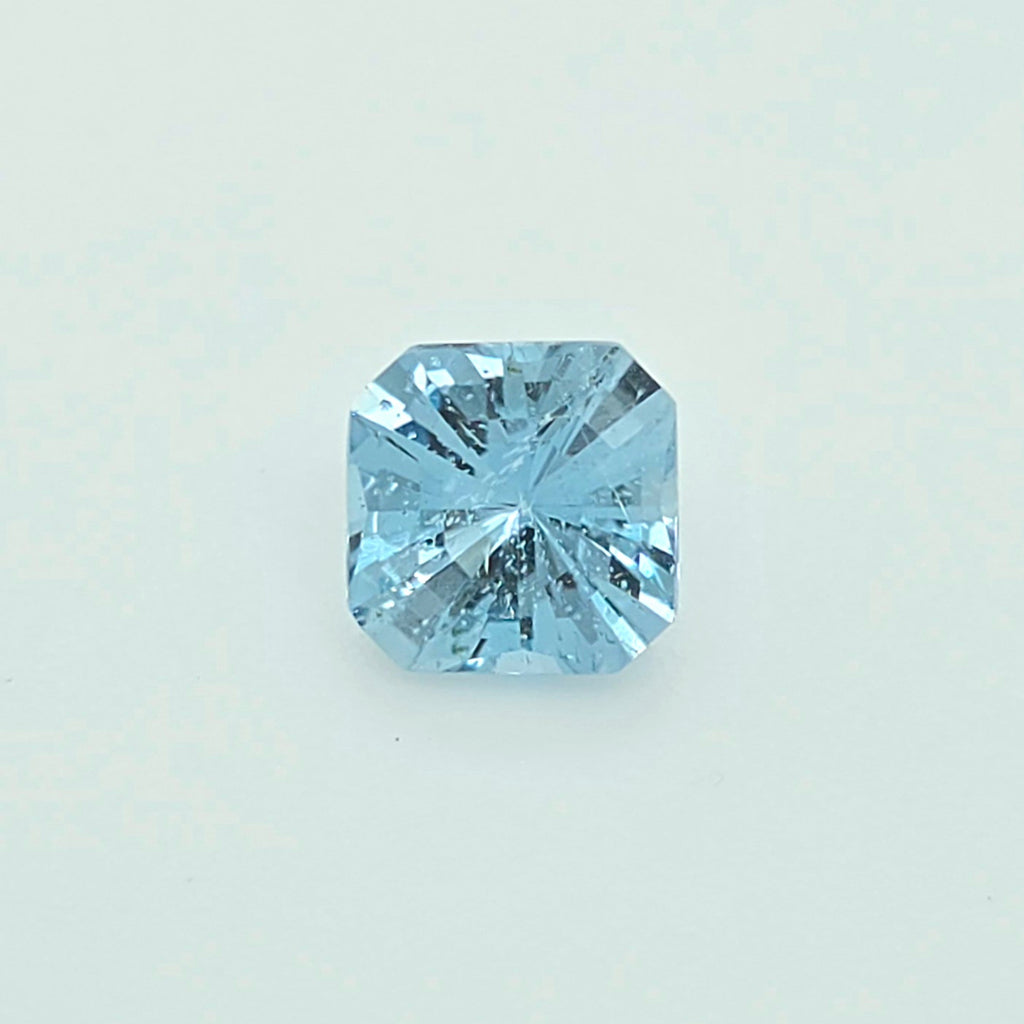A single light blue square-cut gemstone, centered on a clean, pale off-white background.