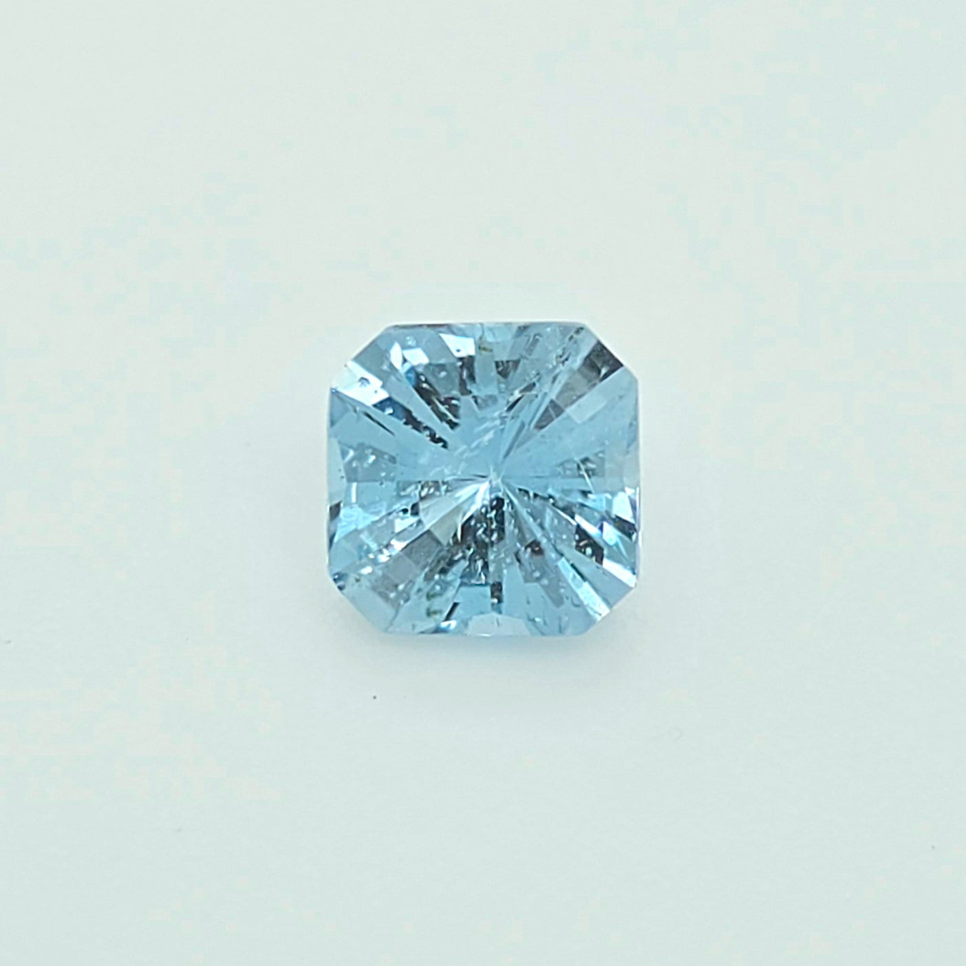 A single light blue square-cut gemstone, centered on a clean, pale off-white background.